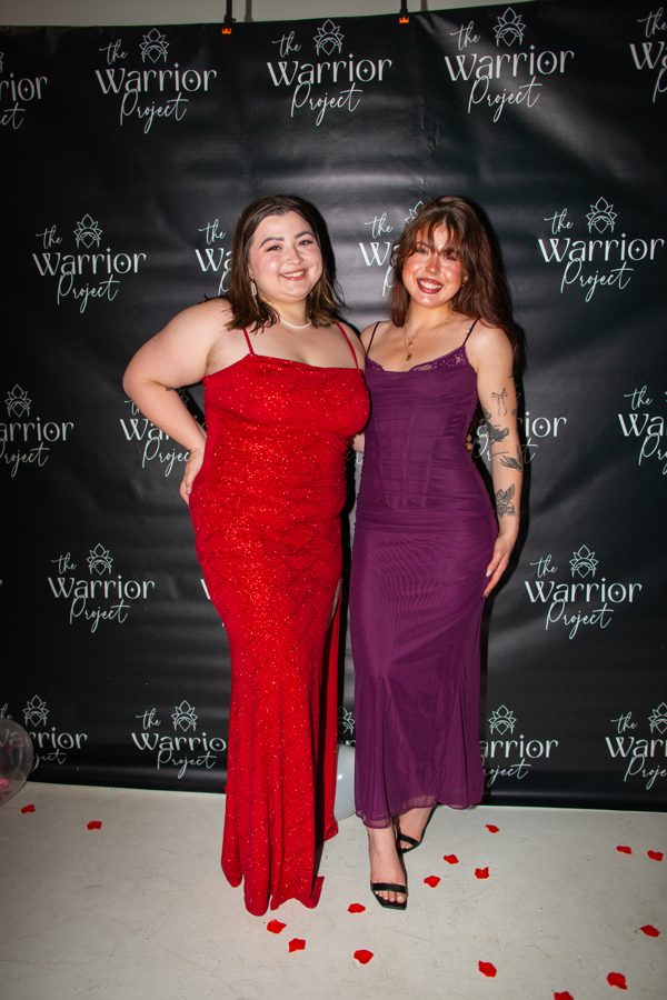 Two members in gowns with rose petals on the Warrior Project backdrop
