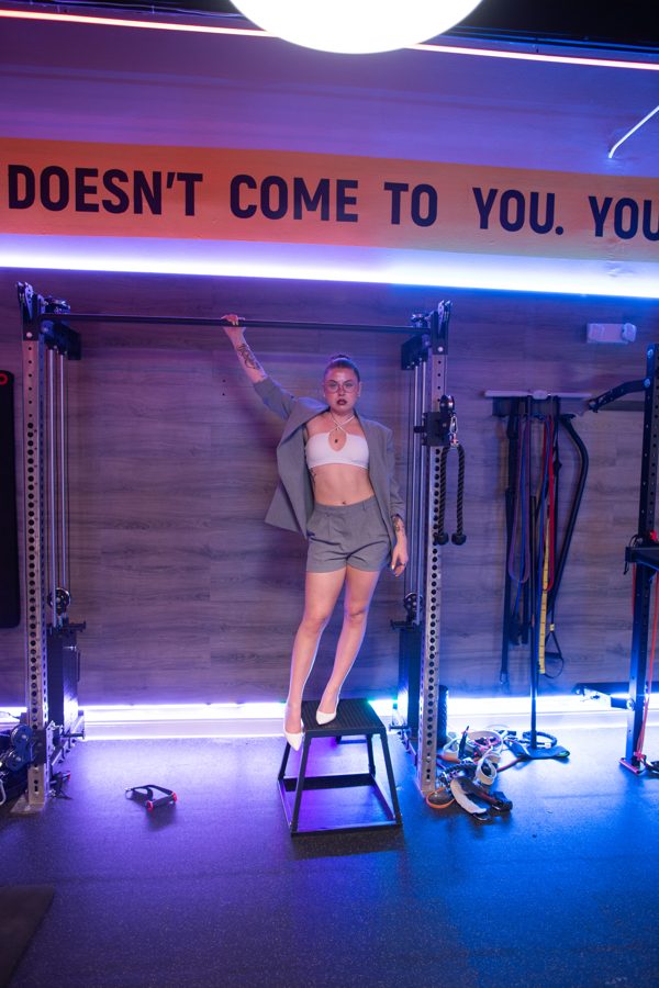 Brie in a blazer and heels posing on a plyo box at the gym