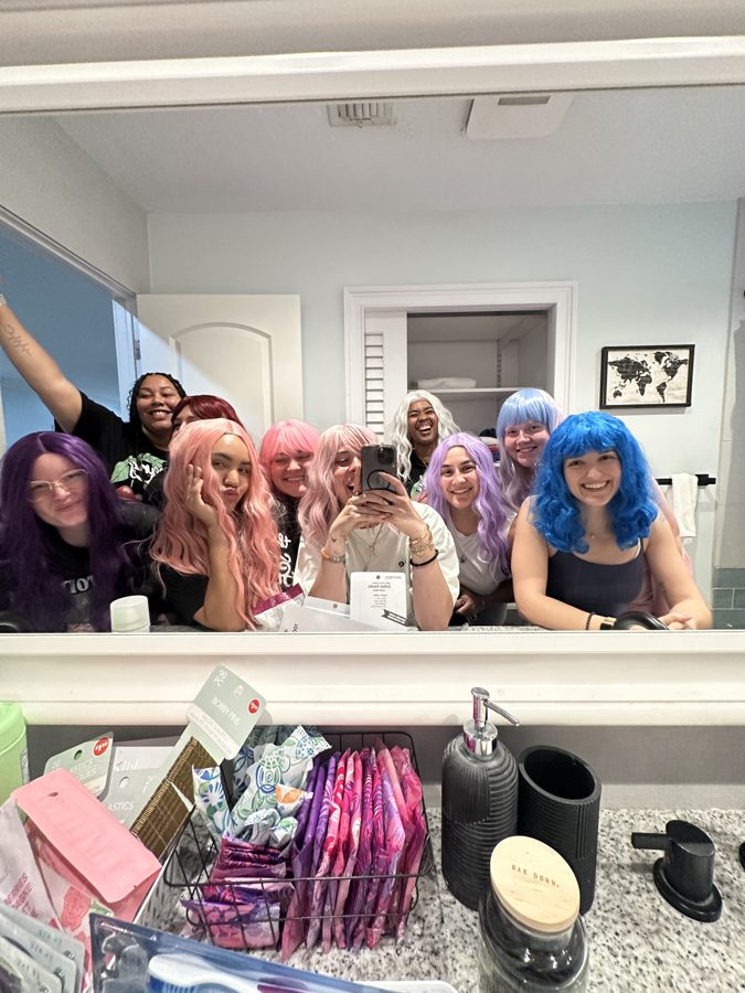 Members in colorful wigs laughing behind a counter
